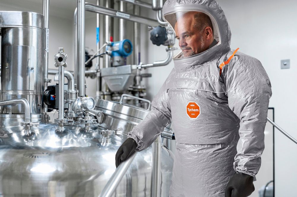 Pharmaceutical female scientist fully dressed in safety equipment seen standing by the machine and holding its cover during production of some drugs very important for human wellbeing during night shift in a pharmaceutical factory.